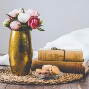 A rustic still life composition with macarons, vintage books, and a flower vase on wooden table.